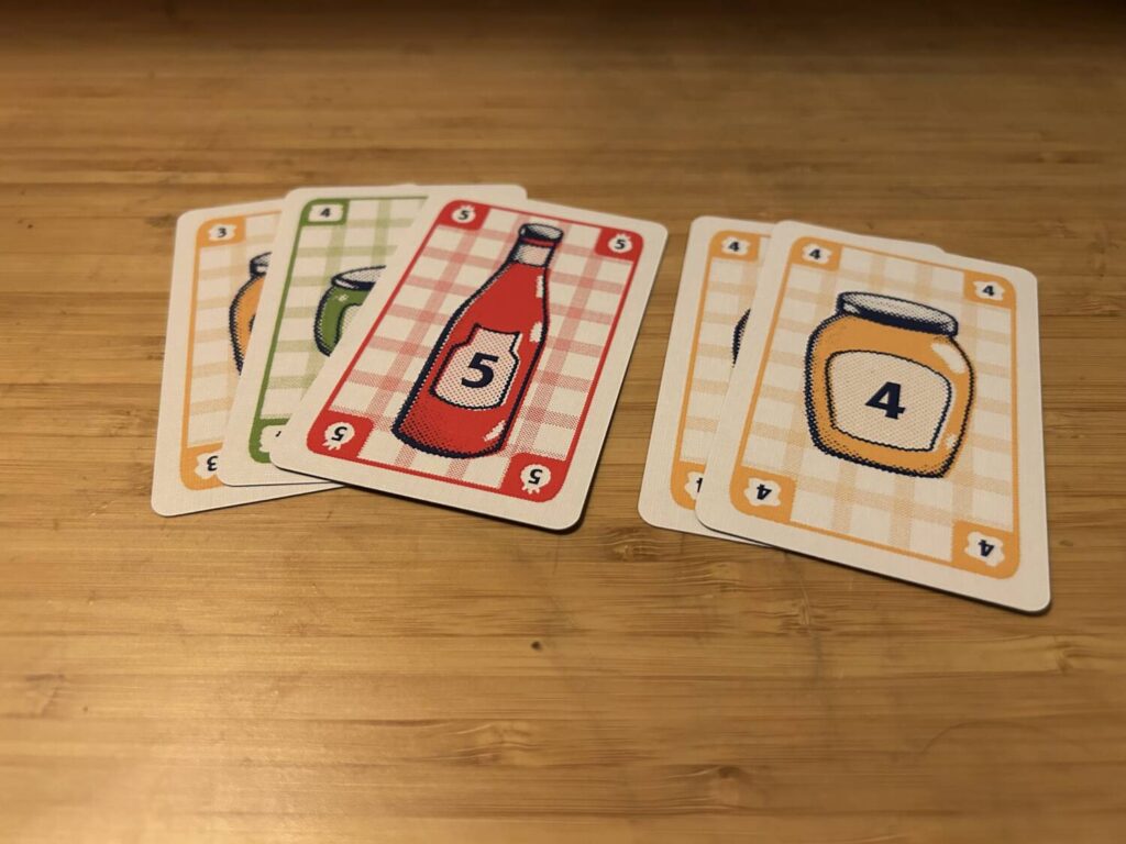 A melded set down on the table, consisting of a three-card, mixed-suit straight and a pair of yellow fours. Each card is decorated with the appropriate condiment bottle.