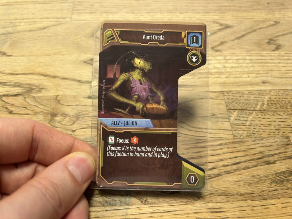 An Ally card from the player deck. It is sleeved, and there is a hexagonal notch cut out of the right side.