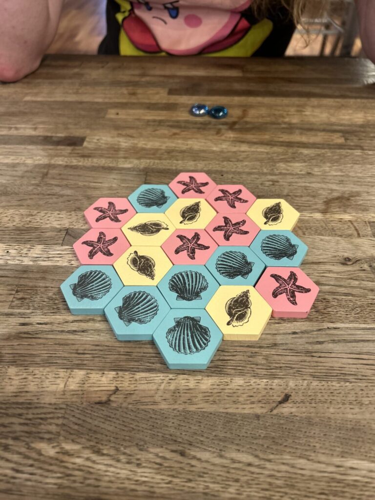 19 hexagons, seven pink, seven teal, and five yellow, in a honeycomb shape on a wooden table.