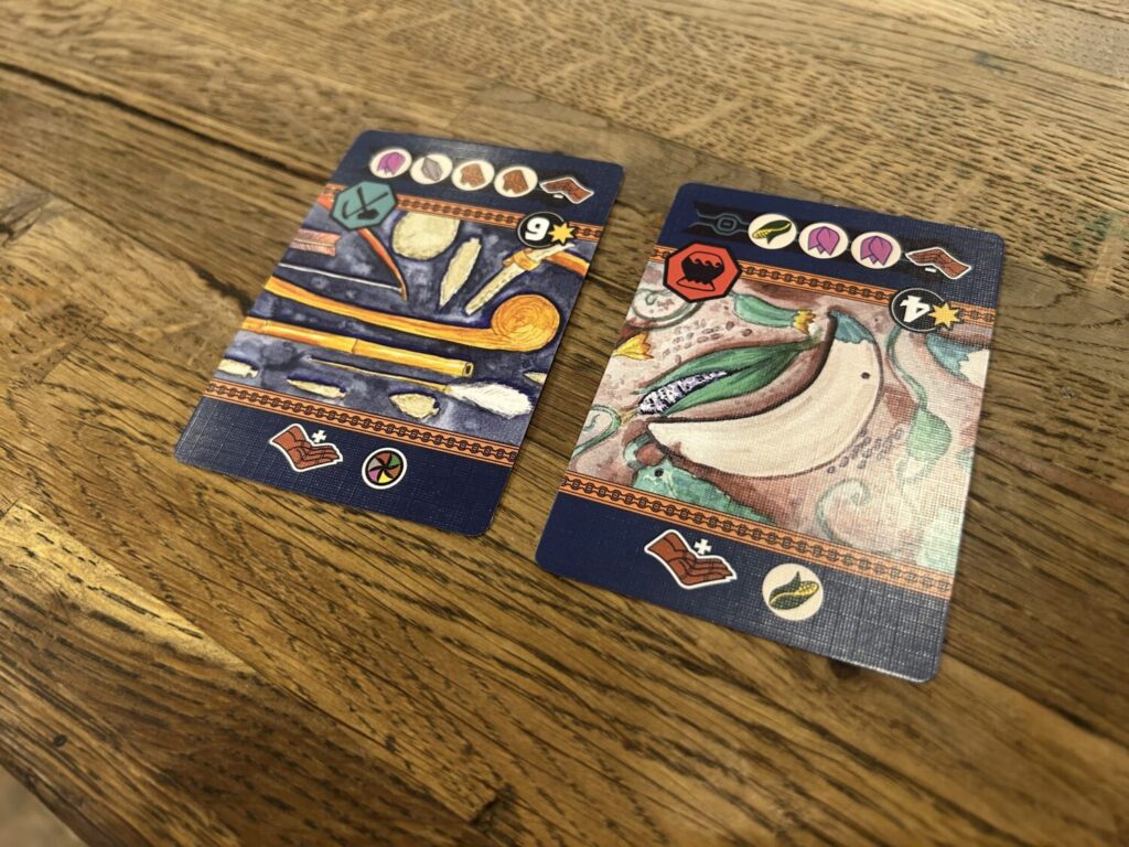 Two task cards. Each includes an illustration in the middle, and two sets of icons. One faces the player who played the card, the other faces the rest of the table.