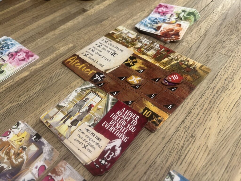 A number of cards and a board sitting on a wooden table. One of the cards, an achievement, is titled "A lover ready to follow you despite everything."