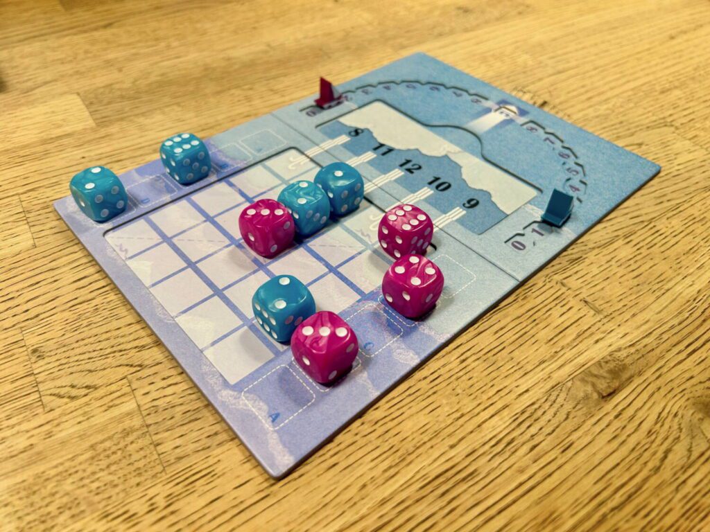 A blue and purple cardboard board, with blue and purple dice on a five-by-five grid, all sitting on a wooden table.