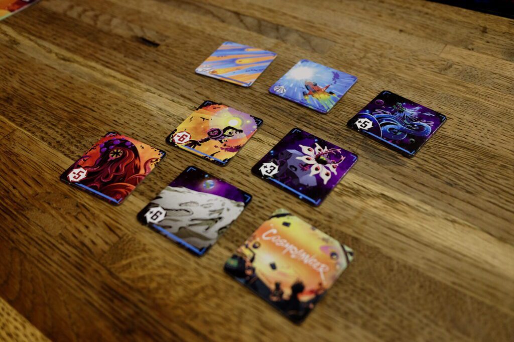A series of tiles laid out on a wooden table. Each and every tile has terrific, colorful, stylized art.