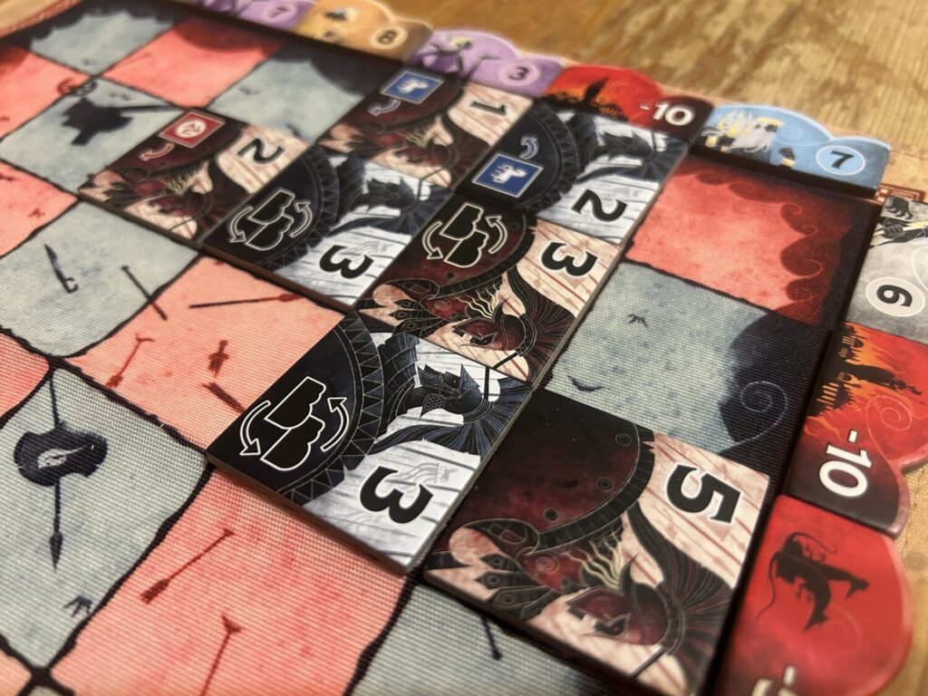 A selection of square titles in red and blue on a cloth mat. Each tile includes an illustration of a Bronze-age soldier and a number.