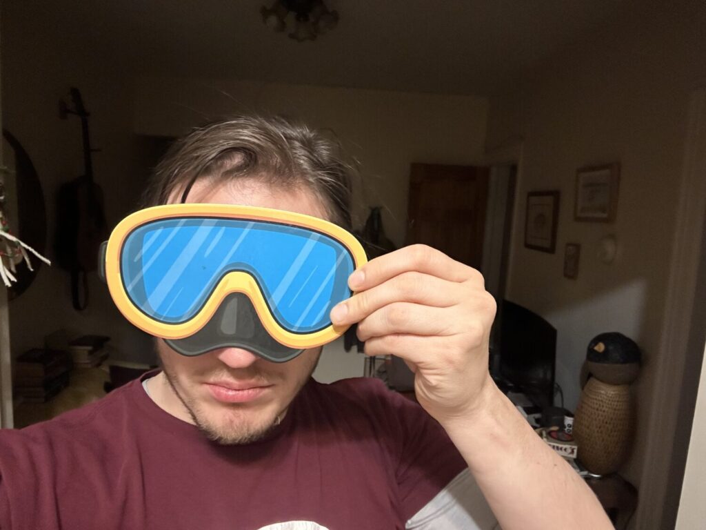 The author of this piece holding a cardboard scuba mask to his face, his eyes covered.