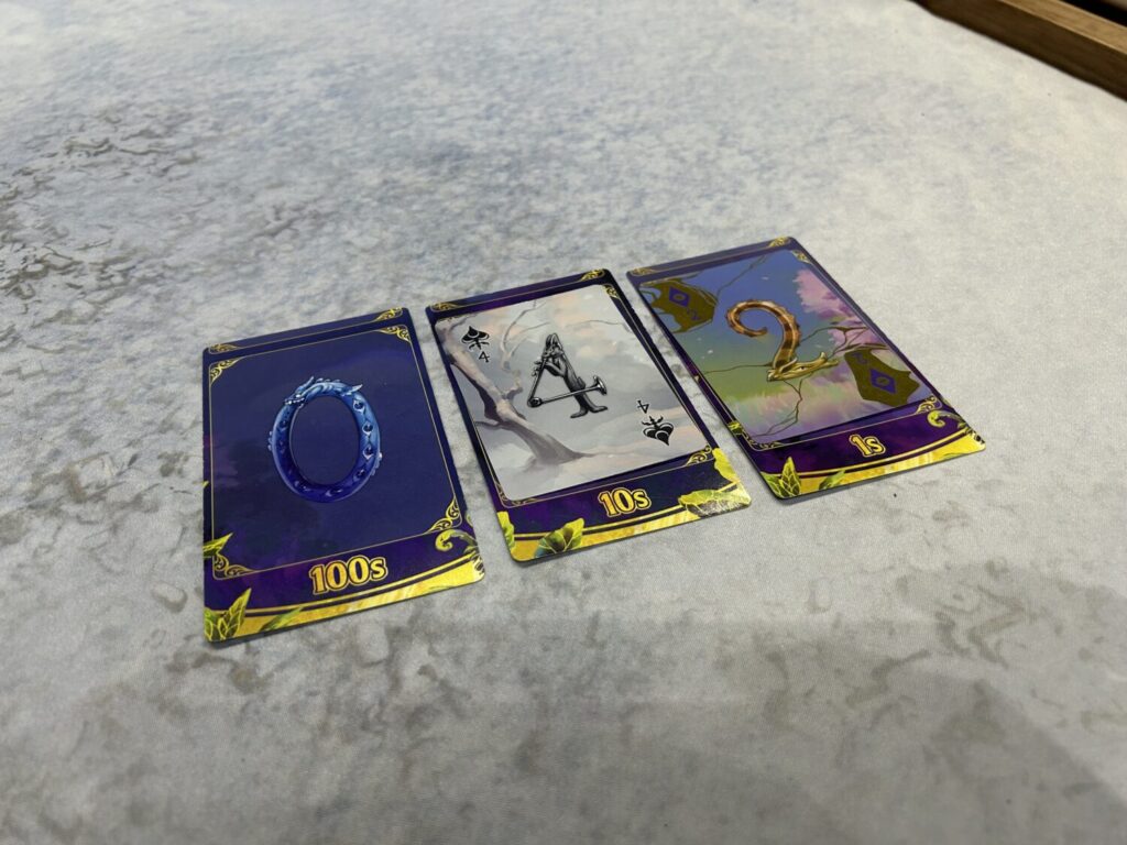 Three tarot-sized cards sit on a table. One shows a zero, and is uncovered. The other two are covered by cards with a "4" and a "2" on them.