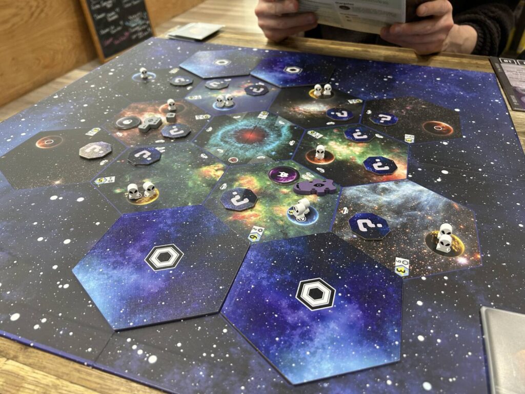 A large board showing deep space, divided into hexagons containing multiple planet tokens.