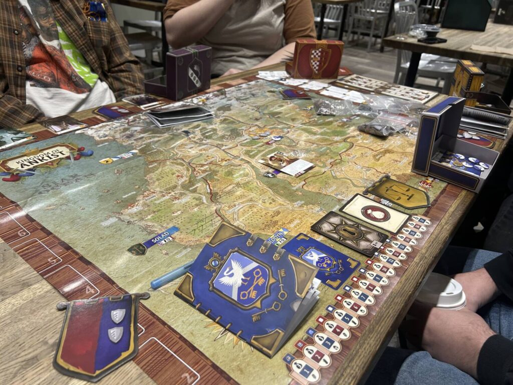 A large paper map fills a table. Each player has in front of them a small treasury box and a player booklet.