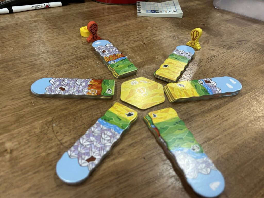 A hexagon with stacks of tiles radiating out from each of its six sides. Wooden balloon markers sit along the outisde.
